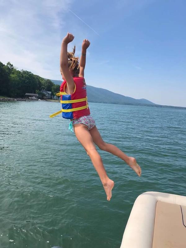 child jumping off of boat into lake
